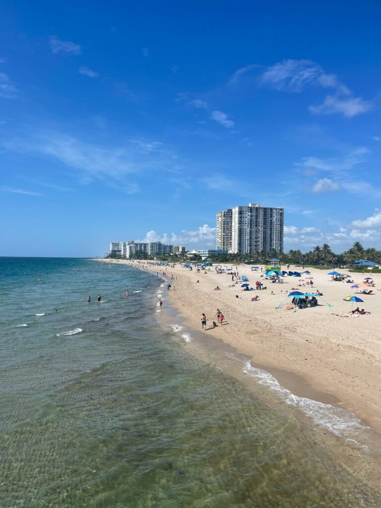 A vibrant beach scene in Florida with skyscrapers, umbrellas, and people enjoying the sun.