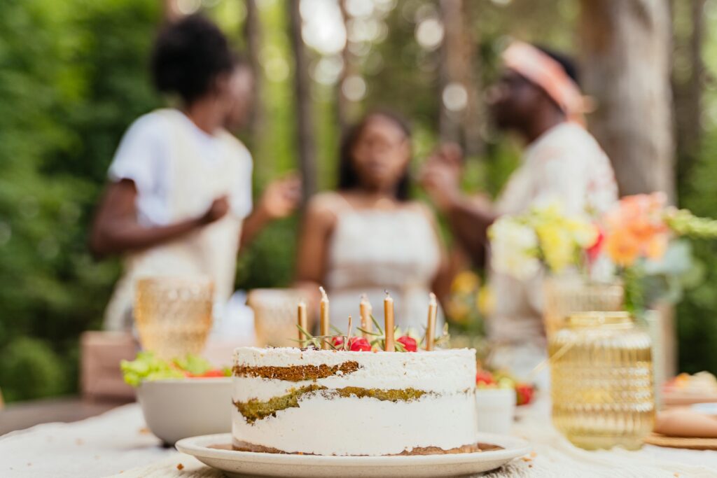 A festive gathering outdoors featuring a decorated cake and blurred figures celebrating.