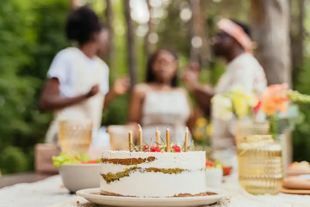 A festive gathering outdoors featuring a decorated cake and blurred figures celebrating.