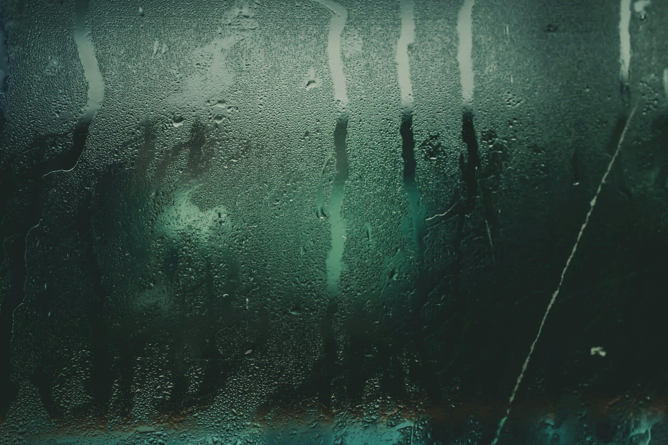 Close-up of a moist glass surface with water droplets and streaks creating an abstract texture.